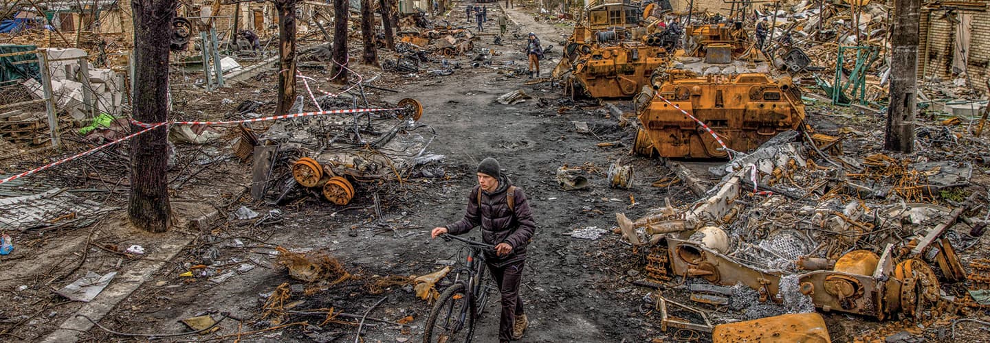 Person with a bicycle walking through a destroyed street with collapsed buildings