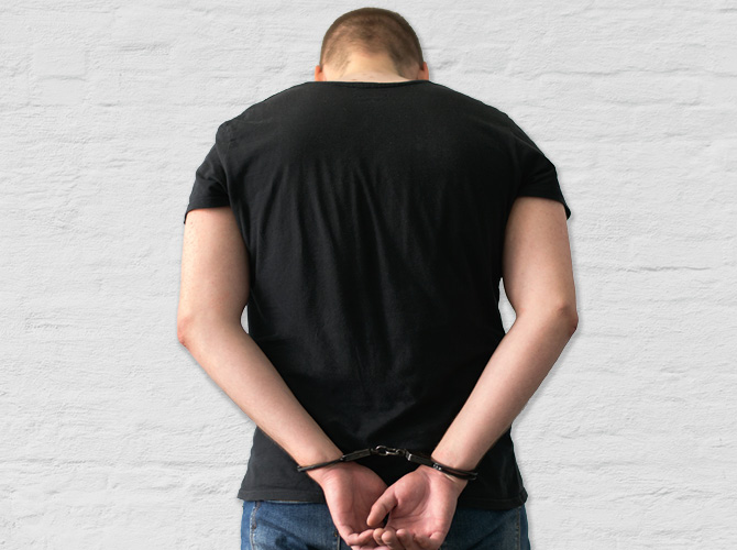 Photo of a person with head lowered and hands cuffed behind their back