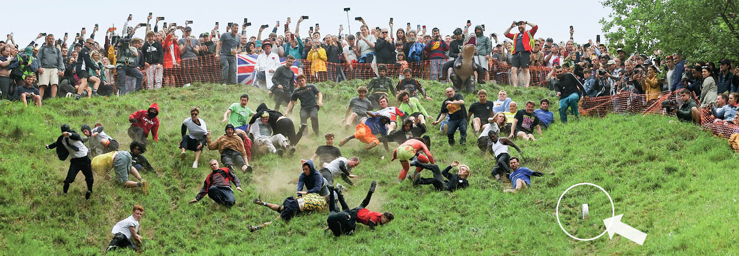 Image of crowd of people rolling down a hill in competition